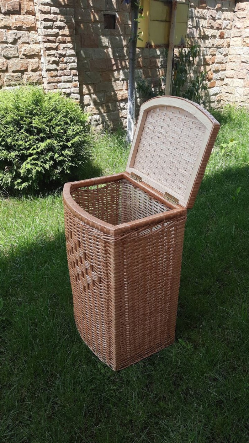 May include: A brown wicker laundry basket with a hinged lid. The lid is open and the basket is sitting on green grass.