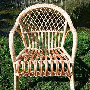 May include: A wicker chair with a woven back and seat. The chair is light brown and has a natural finish. It is sitting on a bed of green grass.