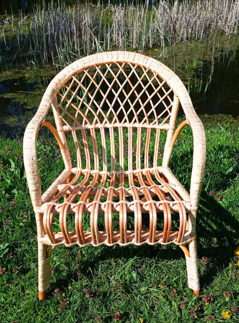 May include: A wicker chair with a woven back and seat. The chair is light brown and has a natural finish. It is sitting on a bed of green grass.