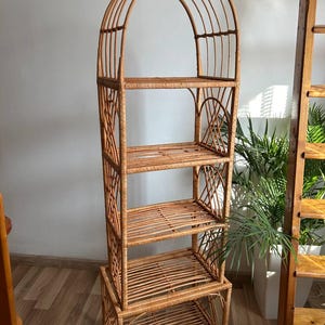 May include: A tall, arched, woven wicker shelf unit with four shelves. The shelf unit is made of natural brown wicker and has a rustic, bohemian style.