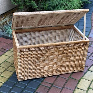 May include: A large, natural woven wicker storage basket with a hinged lid. The lid is open and the basket is empty.