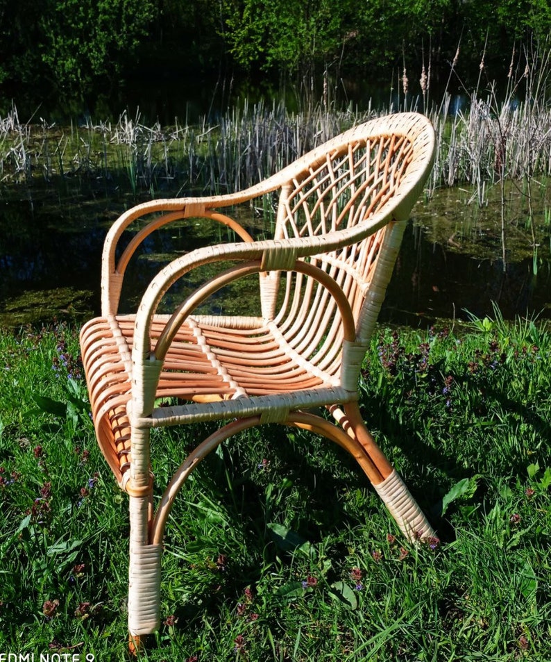 May include: A wicker chair with a natural brown finish. The chair has a high back and arms, and is made of woven rattan. The chair is sitting on a bed of green grass.