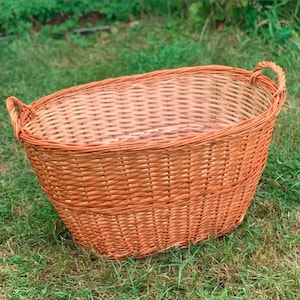 May include: A large, oval-shaped wicker laundry basket with two handles. The basket is made of natural woven wicker and has a light brown color.