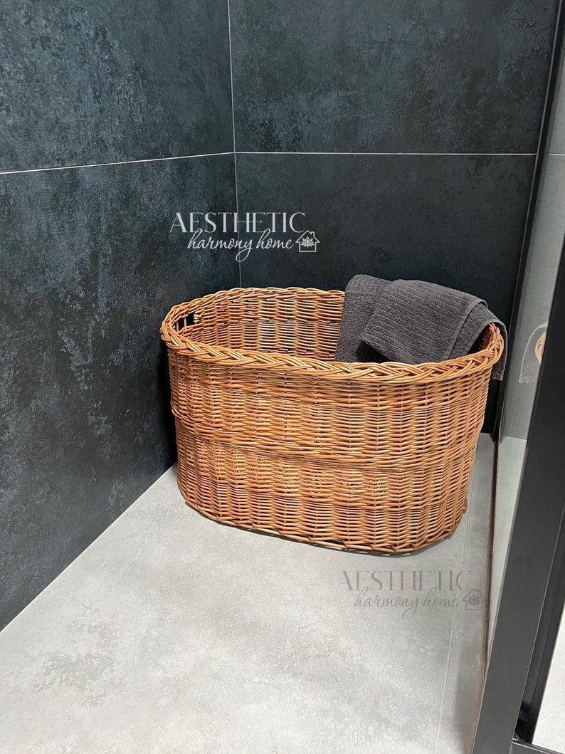 May include: A brown wicker basket with a gray towel inside. The basket is sitting on a gray tiled floor in a bathroom.