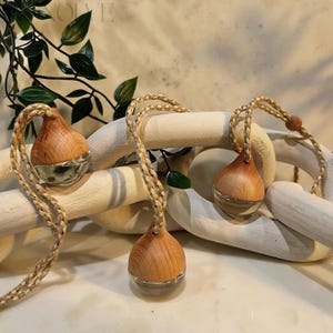 May include: Three wooden teardrop-shaped essential oil diffusers with clear glass bottoms and braided rope hangers. The wooden tops have a light brown color. The diffusers are displayed on a light-colored wooden chain.