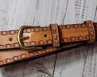 May include: A brown leather belt with an intricate woven design and a brass buckle. The belt is personalized with the initials "MJ".