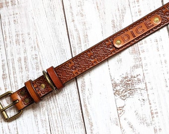 Puede incluir: Un collar de perro de cuero marrón con un diseño de nudo celta y una hebilla de latón. El collar tiene una placa de nombre personalizada que dice "DICE".