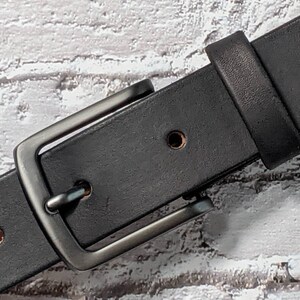 May include: A black leather belt with a silver buckle. The buckle is rectangular with rounded corners and has a smooth, polished finish.