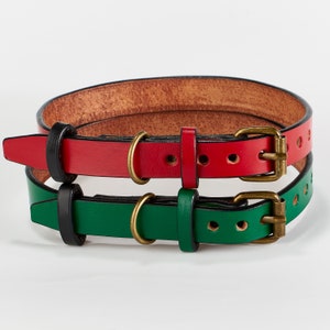 May include: Two leather dog collars, one red and one green, with brass buckles. The collars are stacked on top of each other.
