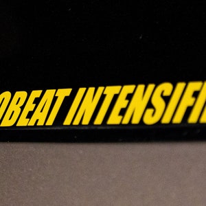 Może przedstawiać: Czarna powierzchnia z tekstem "EUROBEAT INTENSIFIES!" w ż&oacute;łtych literach.