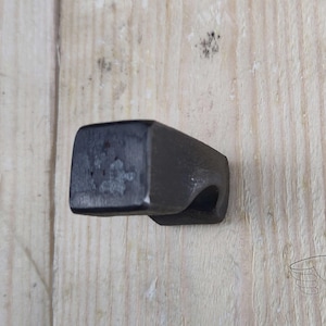 May include: A black metal hook with a square base and a curved hook. The hook is mounted on a wooden surface.