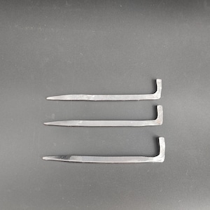 Może przedstawiać: Trzy metalowe łomy z zagiętym końcem i spiczastą końcówką. Narzędzia wykonane są ze srebrnego metalu i ułożone poziomo na ciemnym tle. Narzędzia te służą do podważania i usuwania gwoździ.