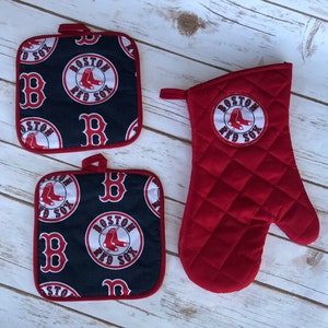 May include: Set of three red and navy blue kitchen pot holders with a Boston Red Sox logo. The pot holders feature a white circle with the words "Boston Red Sox" and a baseball with a pair of red baseball shoes. The pot holders are quilted and have a red trim.
