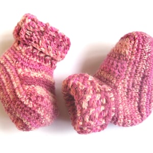 May include: A pair of pink and white knitted baby booties. The booties are made with a soft, textured yarn and have a fold-over cuff.