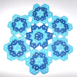 Peut inclure: Un napperon crocheté avec un motif de flocon de neige dans des tons de bleu.