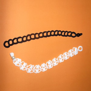 Pode incluir: Duas pulseiras de crochê, uma preta e outra branca, com uma pérola na pulseira branca.