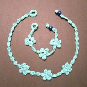 May include: A turquoise crocheted necklace with flower accents and blue beads. The necklace is made of a delicate, lightweight material and features a simple, elegant design.