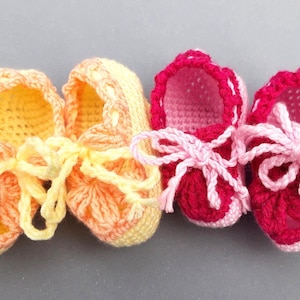 May include: Two pairs of crocheted baby booties. One pair is yellow and orange, the other is pink and red.