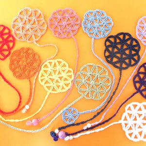 Puede incluir: Una colección de diez marcapáginas de ganchillo en forma de flor en varios colores, incluyendo rojo, naranja, amarillo, verde, azul, morado y blanco. Cada marcapáginas presenta un diseño de flor circular con un borla de cuentas.