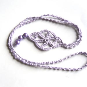 Puede incluir: Un collar de crochet lavanda con un diseño de flor y cuatro cuentas de lavanda.
