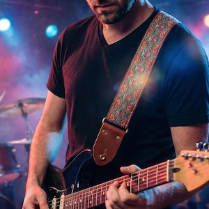 Guitarist playing a black electric guitar on stage with a band using a woven paisley strap. Stylish red and teal embroidery suits professional performances.