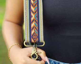 Pode incluir: Uma correia de câmera com padrão preto e branco com um fecho de metal dourado. A correia tem um fundo bege com um padrão geométrico colorido.