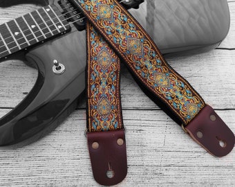 May include: A guitar strap with a brown leather end and a colorful embroidered pattern in shades of blue, gold, and red.