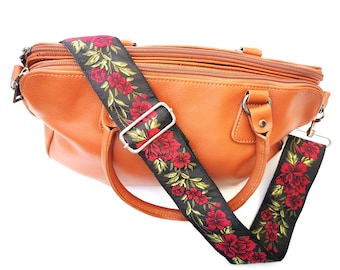 May include: A brown leather handbag with a black and red floral patterned adjustable strap.