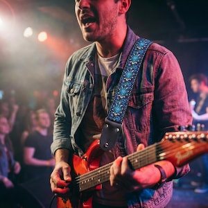 Musician performing live on stage with a red electric guitar and blue embroidered strap. Secure and durable support for energetic rock concerts.