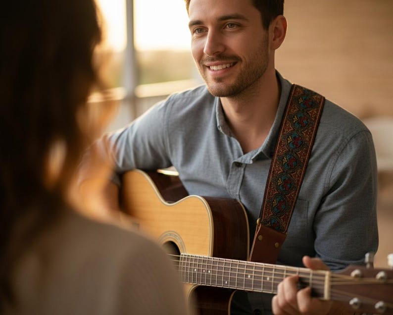 Smiling man playing acoustic guitar using a woven vintage strap during a jam session. Warm red and gold embroidery adds style to a cozy musical moment.