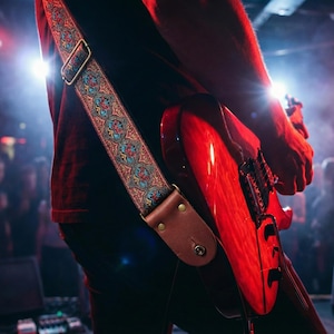 Electric guitarist performing on stage under red lights with a durable woven strap. Colorful vintage embroidery stands out during a live rock concert.