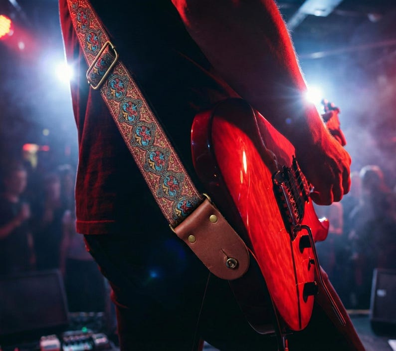 Electric guitarist performing on stage under red lights with a durable woven strap. Colorful vintage embroidery stands out during a live rock concert.