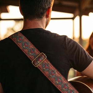 Musician viewed from behind playing acoustic guitar at sunset wearing a comfortable woven strap. Rustic red and gold embroidery fits a country music vibe.
