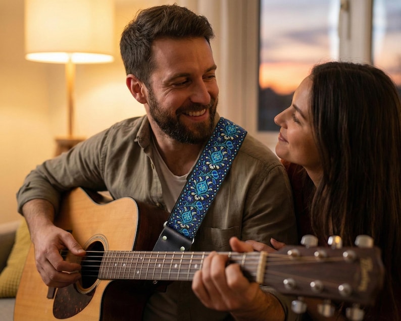 Man playing acoustic guitar at home using a blue patterned strap. Comfortable handmade accessory perfect for cozy indoor practice sessions.