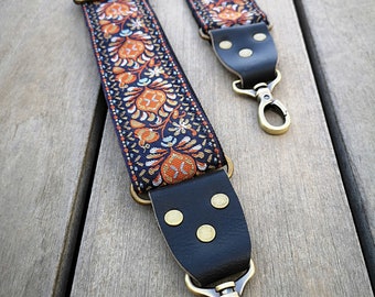 Pode incluir: Uma correia de câmera preta com um padrão floral colorido e detalhes dourados. A correia tem dois fechos de metal.