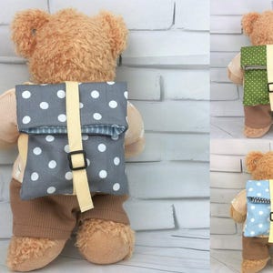 Könnte beinhalten: Drei Teddybären, die verschiedene farbige Rucksäcke mit weißen Punkten tragen. Die Rucksäcke sind aus Stoff und haben einen gelben Gurt. Die Teddybären sind braun und haben braune Nasen.