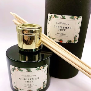 May include: A black glass bottle with a gold lid and wooden sticks, filled with a reed diffuser. The label reads "Smith&Greening Christmas Tree Reed Diffuser Vegan & Cruelty Free 100ml".