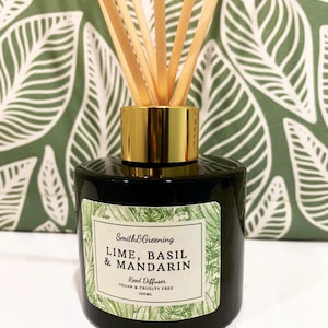 May include: A black glass reed diffuser with a gold-coloured collar and wooden reeds. The label reads "Smith & Greening LIME, BASIL & MANDARIN Reed Diffuser VEGAN & CRUELTY FREE 100ML". The background features a green and white leaf pattern.