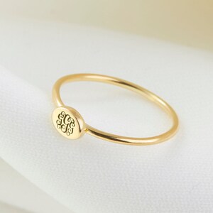 May include: A simple gold band ring with a small, round, engraved monogram on the top.