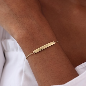 May include: A gold-toned bracelet featuring a thin, polished rectangular bar charm. The bar is engraved with the cursive text I Love You. The charm is attached to a delicate, fine-link chain that secures around the wrist with a simple clasp mechanism.