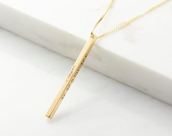 Puede incluir: Un collar con colgante de barra vertical en tono dorado con una cadena delicada. La barra rectangular está grabada con texto en cursiva y las coordenadas 33 52' S 151 12' E, suspendida de una fina cadena que capta la luz.