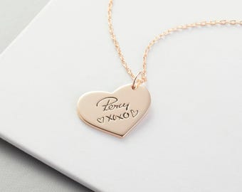May include: A rose gold heart-shaped pendant necklace featuring the engraved name Percy followed by XOXO and two small heart symbols. The pendant hangs from a delicate matching rose gold chain, showcasing a polished metallic finish.