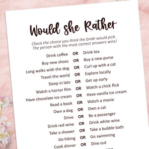 May include: A white paper game titled "Would She Rather" with a list of choices for a bridal shower. The game includes questions like "Drink coffee OR Drink tea" and "Buy new shoes OR Buy a new purse."