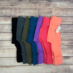 May include: A set of eight pairs of leggings in various colors, including black, gray, green, blue, purple, pink, and orange. The leggings are made of a soft, stretchy fabric and have a comfortable fit. The tag on the orange leggings reads "Coco Cash".
