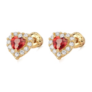 May include: A pair of gold-colored heart-shaped stud earrings. Each earring features a vibrant red center stone surrounded by a halo of small, clear gemstones. The earrings have a classic, elegant design.