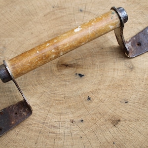 May include: A rustic wooden handle with metal brackets, likely used as a door or cabinet pull. The handle is worn and shows signs of age, with a natural wood finish and metal that has rusted.