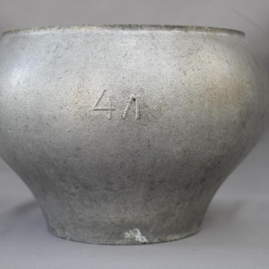 May include: A large, round, silver-coloured metal pot with a wide mouth and a slightly tapered base. The number "41" is etched into the side. The pot has a textured surface and a vintage appearance.