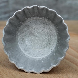 May include: A silver metal pie pan with a fluted edge. The pan is empty and has a smooth, shiny surface.