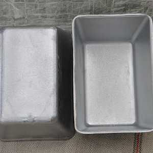 Może przedstawiać: Dwa srebrne metalowe foremki do chleba. Formy są prostokątne i mają gładką, błyszczącą powierzchnię.