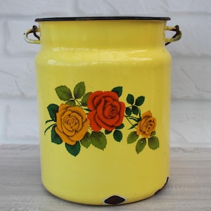 Puede incluir: Cubo de leche de esmalte amarillo con un diseño floral con rosas rojas, naranjas y amarillas. El cubo tiene dos asas de metal.